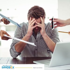 image of man at a desk with his head in his hands and a laptop and several people handing him work to do showing mistakes leaders make