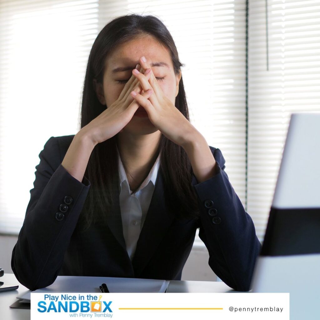 image of a woman at a desk with a monitor with her hands over her face. she is quiet quitting