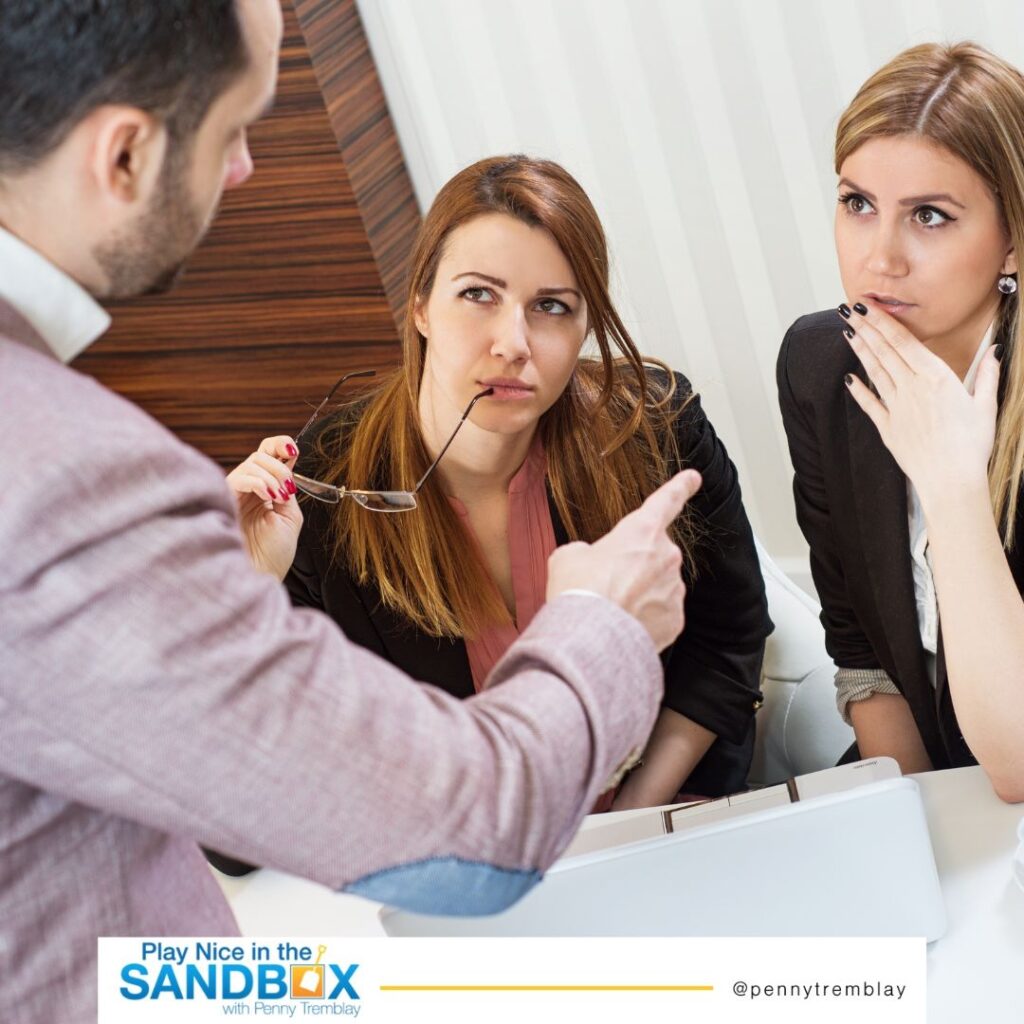 image of a male boss pointing his finger at one of two female co-workers giving her public criticism