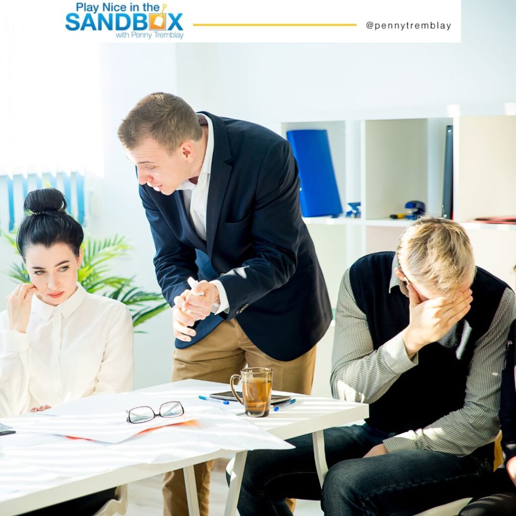 image of a boss giving public criticism to a female employee while a male employee looks away covering his face with his hand