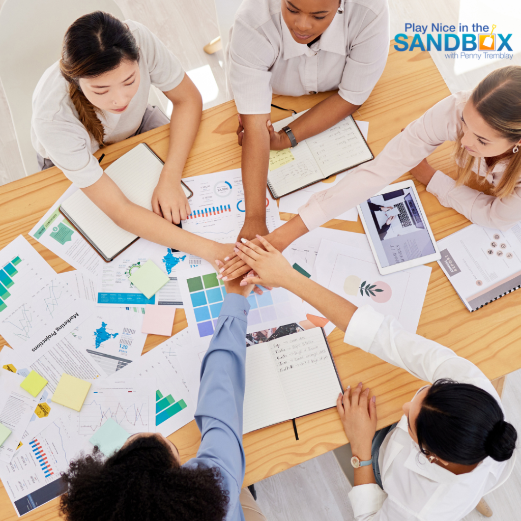 image of a group of coworkers st a desk with several papers on the desk and they have their hands in the center of the table on top of each other to signify effective team conflict resolution