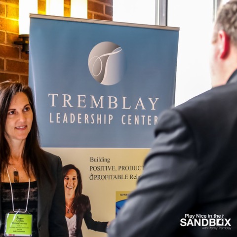 image of Penny Tremblay speaking to a gentleman about listening at a conference in front of her Tremblay Leadership Centre poster