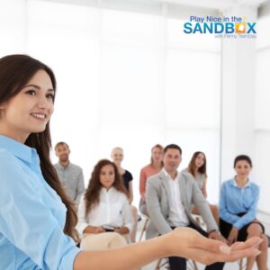 image of a woman standing with her hand outstretched in front of a group of coworkers sitting in an audience to show how Managing Team Conflict: 5 Strategies for HR to Ease Employee Tensions can become a reality